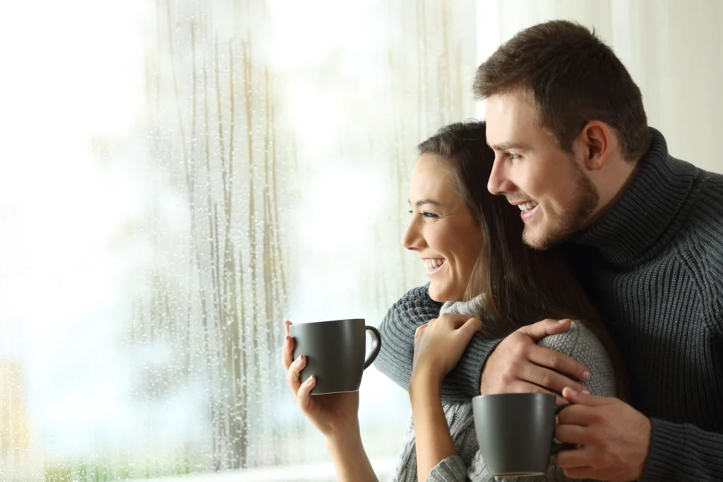 couple drinking coffee in front of home window during rain storm